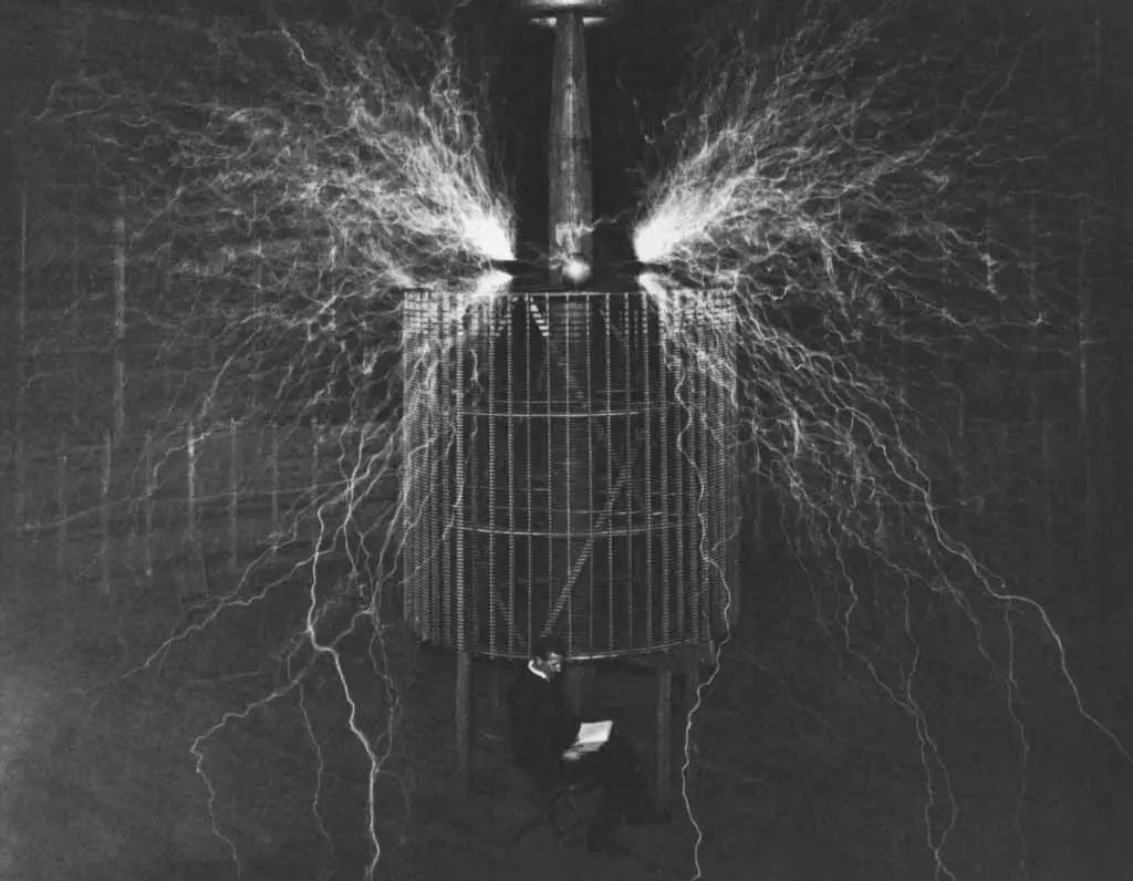  A glow of nitrogen fills the atmosphere. Tesla is photographed sitting in front of his generator. This photograph was taken in 1899.